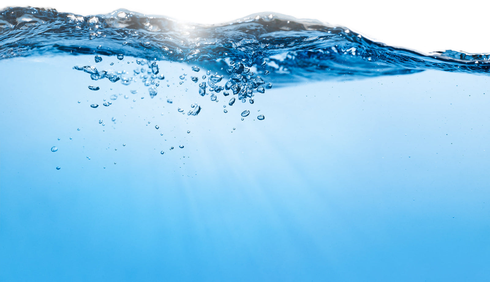 Close-up of clear blue water with a visible surface ripple, bubbles rising through the water, and bright light filtering down from above.